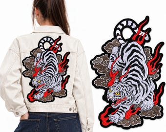 Peut inclure: Une veste en jean blanc avec un grand écusson brodé dans le dos. L'écusson représente un tigre blanc aux rayures noires, aux yeux jaunes et à la gueule ouverte, entouré de nuages gris foncé stylisés et de flammes rouges vives.