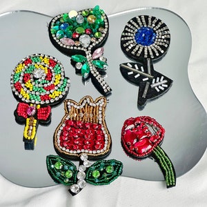May include: Six colorful embroidered iron-on patches featuring a lollipop, a flower, a tulip, a strawberry, and two different flower designs.