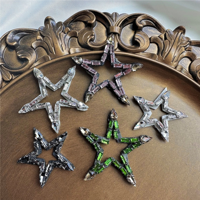 Peut inclure: Cinq embellissements en forme d'&eacute;toile avec des strass de diff&eacute;rentes couleurs. Les &eacute;toiles sont faites d'un mat&eacute;riau transparent et pr&eacute;sentent une vari&eacute;t&eacute; de couleurs, notamment l'argent, le noir, le vert et le violet.