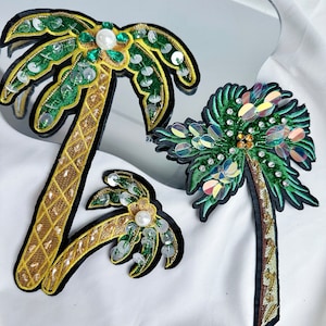 May include: Two green and gold palm tree iron-on patches with sequins and beads. The palm trees are on a white fabric background.