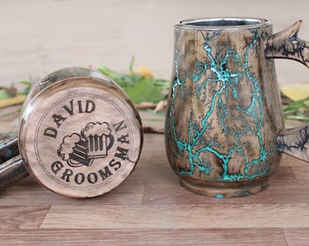 Könnte beinhalten: Zwei Bierkrüge aus Holz. Ein Krug steht aufrecht, der andere liegt auf der Seite. Der aufrechte Krug hat einen Griff und türkisfarbene Akzente. Der Boden des anderen Kruges trägt den Text "DAVID GROOMSMAN" und eine Bierkrug-Grafik.