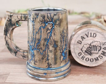 Könnte beinhalten: Ein hölzerner Bierkrug mit metallischem Innenraum und Henkel, verziert mit schwarzen Fraktal-Brandmustern, die mit leuchtend blauem Harz gefüllt sind. Daneben liegt ein runder Holzuntersetzer mit der Gravur DAVID GROOMSMAN und zwei Bierkrügen.