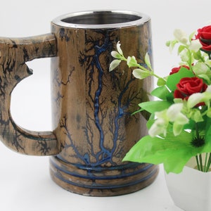 May include: A cylindrical wooden mug featuring a metallic interior lining and a large handle. The exterior surface displays a natural brown wood grain with dark, branching fractal patterns and inlaid blue resin accents throughout the design.