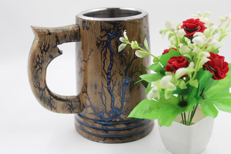 May include: A cylindrical wooden mug featuring a metallic interior lining and a large handle. The exterior surface displays a natural brown wood grain with dark, branching fractal patterns and inlaid blue resin accents throughout the design.