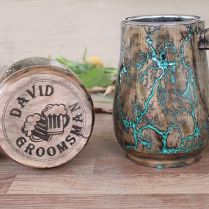 Può includere: Due boccali di birra in legno. Un boccale è sdraiato su un lato, mostrando il testo inciso "DAVID GROOMSMAN" e una grafica di boccale di birra. L'altro boccale è in posizione verticale, con un motivo unico a fulmini turchesi.