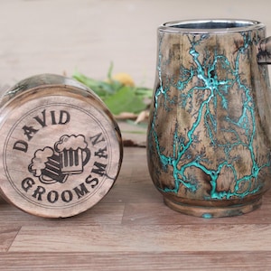 Può includere: Due boccali di birra in legno. Un boccale è sdraiato su un lato, mostrando il testo inciso "DAVID GROOMSMAN" e una grafica di boccale di birra. L'altro boccale è in posizione verticale, con un motivo unico a fulmini turchesi.