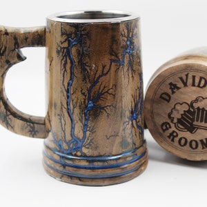 May include: A wooden beer mug with a stainless steel interior and a handle, featuring dark brown wood grain with blue fractal lightning patterns. Beside it lies a matching wooden lid engraved with the text DAVID GROOMSMAN and two beer mugs.
