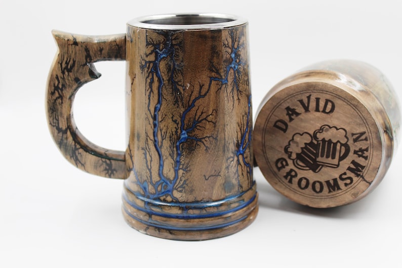 May include: A wooden beer mug with a stainless steel interior and a handle, featuring dark brown wood grain with blue fractal lightning patterns. Beside it lies a matching wooden lid engraved with the text DAVID GROOMSMAN and two beer mugs.
