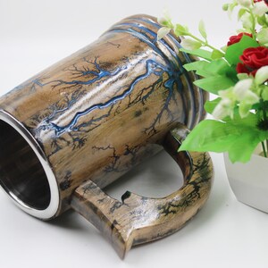 May include: A cylindrical mug with a polished silver-toned metal interior and a wooden exterior featuring dark, branching fractal patterns filled with a vibrant blue resin inlay. The mug has a sturdy wooden handle and a smooth, glossy finish.