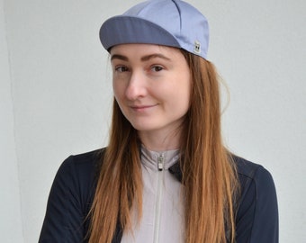 May include: A woman wearing a light blue cycling cap with a black zippered jacket and a light gray shirt.