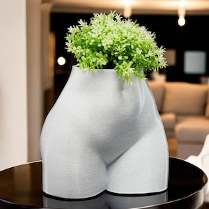 May include: White ceramic planter shaped like a human body, with a small green plant growing out of the top.