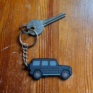 May include: A black rubber keychain shaped like a car. The keychain has a silver key ring and chain.