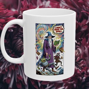 May include: White ceramic mug featuring a colorful illustration of a wizard, a frog in armor, and a raccoon. The wizard wears a purple robe and blue hat, holding a spell book. Text reads "I DIDN'T READ THE SPELL".