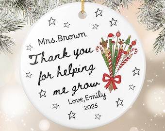 May include: White ceramic Christmas ornament with gold string, featuring the text "Mrs. Brown, Thank you for helping me grow, Love, Emily, 2025." Decorated with stars and a bouquet of pencils, candy canes, and Christmas tree designs.