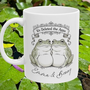 May include: White ceramic mug featuring two cartoon frogs kissing, with the text "We Deleted the Apps" above them. Below the frogs, the names "Emma & Benny" are written in cursive.