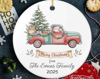 May include: A round Christmas ornament featuring a red and green vintage truck carrying a Christmas tree and gifts. Santa Claus is in the driver's seat. The ornament has the text "Merry Christmas from The Evans Family 2025".