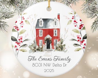May include: A white ceramic Christmas ornament with a red house illustration. The house has a gray roof and a black door. The ornament is decorated with greenery and berries, and includes the text "The Evans Family" and address information.