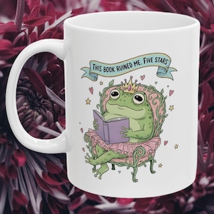 May include: White ceramic mug featuring a cartoon frog wearing a crown and tutu, reading a book while seated on a decorative chair. The mug has the text "THIS BOOK RUINED ME. FIVE STARS" on a banner.