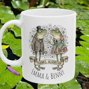 May include: White ceramic mug featuring a whimsical illustration of two anthropomorphic frogs. One frog wears a suit and top hat, the other a dress and crown. The mug has the text "THANKS, ALGORITHM" and "EMMA & BENNY".