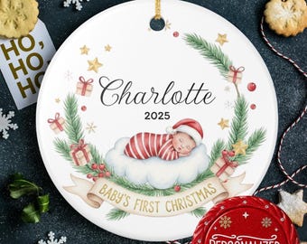 May include: White ceramic Christmas ornament with a baby design. The ornament features the name "Charlotte" and the year "2025". A sleeping baby in a Santa hat is on a cloud, surrounded by festive elements. The banner reads "Baby's First Christmas".
