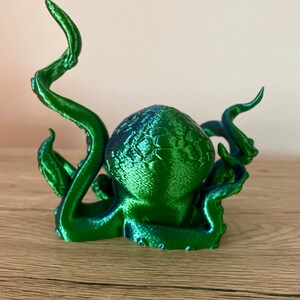 May include: A 3D printed green octopus figurine with a textured surface. The octopus has eight tentacles, some of which are curled up.