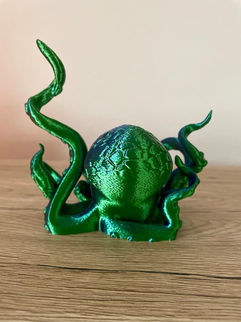 May include: A 3D printed green octopus figurine with a textured surface. The octopus has eight tentacles, some of which are curled up.