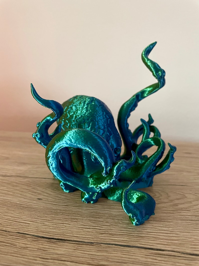 May include: A 3D printed octopus figurine with a blue and green iridescent finish. The octopus has eight tentacles and is curled up in a defensive position.