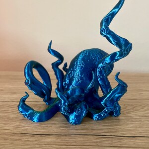 May include: A blue 3D printed octopus figurine with detailed tentacles. The octopus is sitting on a wooden surface.