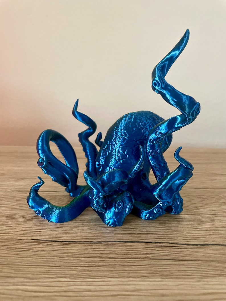 May include: A blue 3D printed octopus figurine with detailed tentacles. The octopus is sitting on a wooden surface.