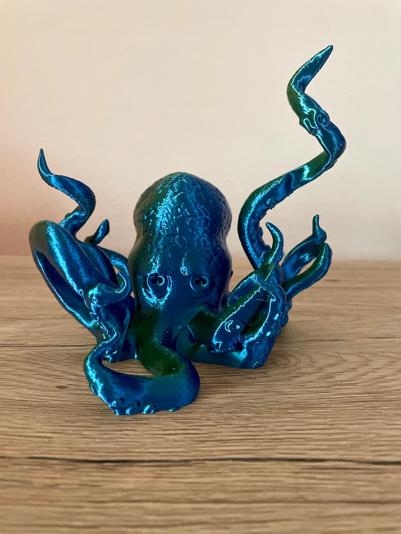 May include: A 3D printed octopus figurine with a blue and green iridescent finish. The octopus has eight tentacles and is posed in a sitting position.