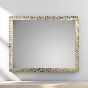 Op de afbeelding: Rechthoekige spiegel met een getextureerde, goudkleurige lijst. De spiegel staat tegen een witte muur en reflecteert de kamer. De lijst heeft een ruwe, organische textuur, wat visuele interesse aan het ontwerp toevoegt. De algehele esthetiek is modern en elegant.