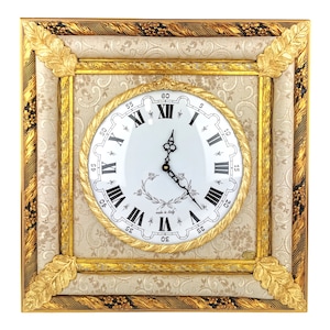 May include: A square wall clock with a gold frame and a white face. The clock has Roman numeral markings and a black hour and minute hand. The clock face has a gold rope design around the edge and the words "Made in Italy" in the center.