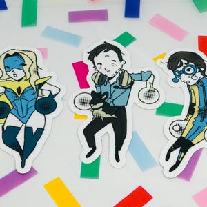 Könnte beinhalten: Drei gestanzte Aufkleber mit Zeichentrickfiguren. Einer ist eine Superheldin in Blau und Gelb. Der zweite ist ein Mann in einem blauen Hemd, der ein kleines schwarzes Tier hält. Der dritte ist eine Person in einem blau-gelb gestreiften Anzug.