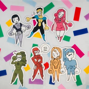 Op de afbeelding: Een verzameling van zeven stickers met superhelden. Elke sticker toont een uniek karakterontwerp met gedurfde contouren en levendige kleuren. De stickers zijn geplaatst tegen een achtergrond van kleurrijke confetti.