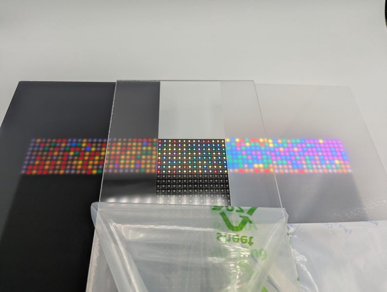 Pode incluir: Uma cole&ccedil;&atilde;o de pain&eacute;is transparentes e opacos, cada um exibindo uma grade de luzes LED coloridas. Os pain&eacute;is variam em cor, incluindo preto, transparente e fosco, com as luzes emitindo um espectro de tons. Um saco pl&aacute;stico est&aacute; em primeiro plano.