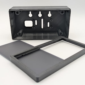 May include: A black rectangular plastic enclosure consisting of a deep base with internal mounting screw holes and keyhole slots, paired with a separate flat cover frame featuring a large rectangular opening and a solid rectangular panel section.