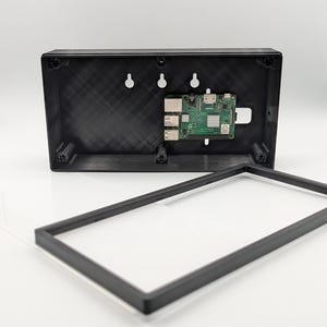 May include: A black rectangular plastic enclosure for a single-board computer, featuring a mounted green circuit board with various ports and a separate black rectangular frame that serves as a cover for the device housing assembly.