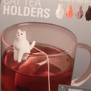 Puede incluir: Conjunto de cuatro soportes para té con forma de gato. Los soportes están hechos de silicona y tienen forma de gato en varios colores, incluyendo blanco, naranja, gris y negro. Los soportes están diseñados para sujetar las bolsitas de té en una taza.