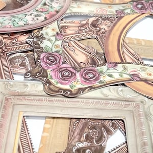 May include: A selection of decorative paper frames in assorted shapes and sizes. The frames showcase elaborate designs with floral and scrollwork patterns in pink, brown, and cream hues. Some frames have a distressed, vintage appearance.