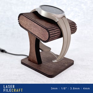 May include: A wooden watch stand with a dark brown finish. The stand is designed to hold a smartwatch with a band. The stand has a slot for charging the watch. The stand is made of 3mm thick wood.