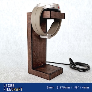 May include: A wooden watch stand with a charging cable. The stand is dark brown and has a slot for the watch band. The watch is silver and has a black band.