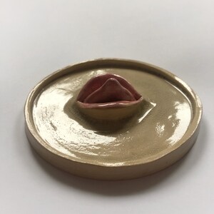 Pode incluir: Um prato de cer&acirc;mica com um design em relevo em forma de l&aacute;bio rosa no centro. O prato &eacute; de cor bege claro e tem um acabamento brilhante.