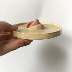 Pode incluir: Um prato de cer&acirc;mica com um design de l&aacute;bios rosados em relevo. O prato &eacute; bege claro e tem um acabamento brilhante.