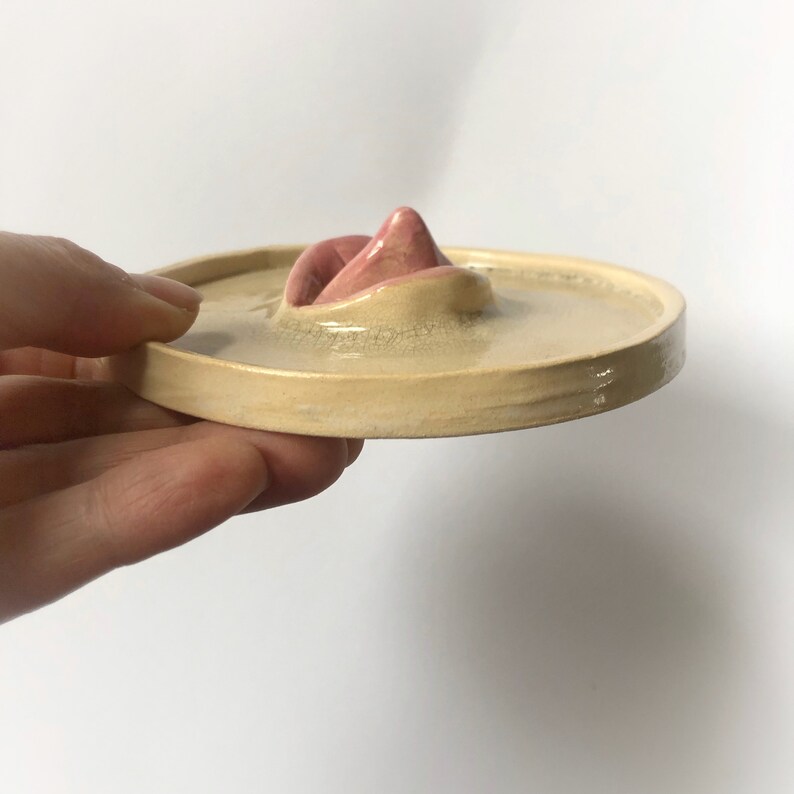 Pode incluir: Um prato de cer&acirc;mica com um design de l&aacute;bios rosados em relevo. O prato &eacute; bege claro e tem um acabamento brilhante.