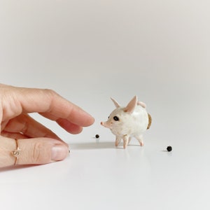 Puede incluir: Una figurita de cer&aacute;mica blanca de un animal peque&ntilde;o con orejas grandes y cuerpo redondo. La figurita tiene un tap&oacute;n de corcho en la espalda y est&aacute; de pie sobre una superficie blanca.