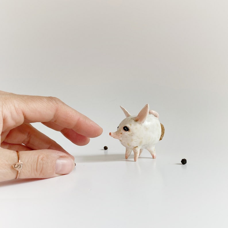 Puede incluir: Una figurita de cer&aacute;mica blanca de un animal peque&ntilde;o con orejas grandes y cuerpo redondo. La figurita tiene un tap&oacute;n de corcho en la espalda y est&aacute; de pie sobre una superficie blanca.