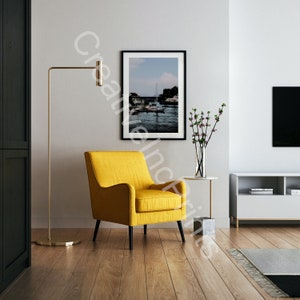 Pode incluir: Uma poltrona amarela com pernas pretas fica em uma sala de estar com uma fotografia emoldurada de uma cena de porto, um vaso de flores cor-de-rosa e um centro de entretenimento branco com uma televisão preta.