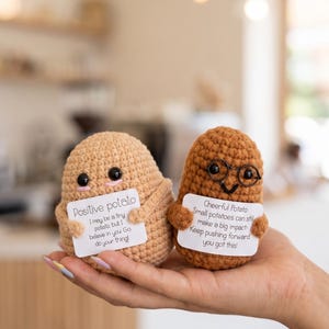 May include: Two crocheted potato figures, one light tan and one brown, each holding a white card. The tan potato says Positive potato, I may be a tiny potato, but I believe in you Go do your thing! The brown potato wears glasses and says Cheerful Potato, Small potatoes can still make a big impact! Keep pushing forward you got this!