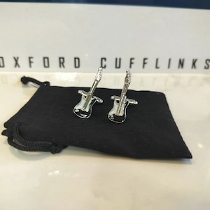 May include: A pair of silver guitar cufflinks in a black velvet pouch. The pouch has a drawstring closure and the text "OXFORD CUFFLINKS" is printed on the top.