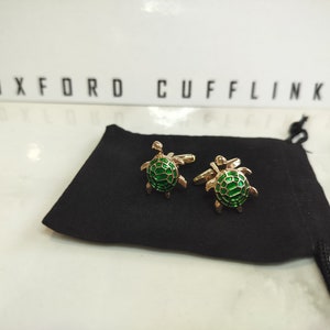May include: A pair of gold turtle cufflinks with green enamel. The cufflinks are in a black velvet pouch.